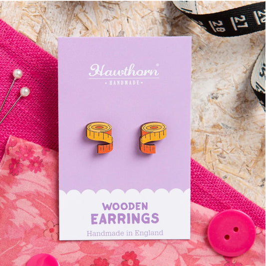 Wooden earrings on a purple card with 'Hawthorn Handmade' branding, surrounded by pink fabric and sewing tools.