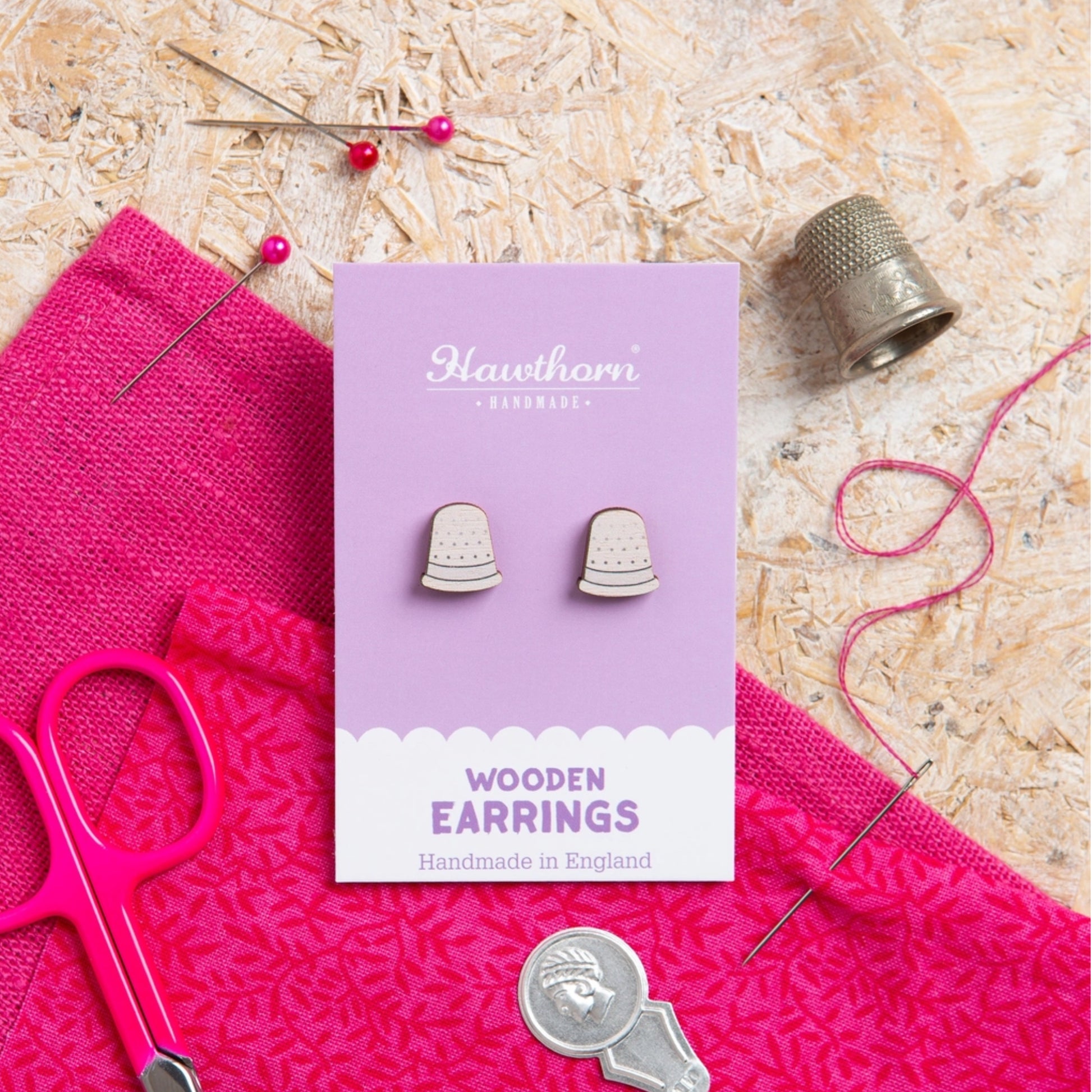 Pair of wooden earrings on a purple card with sewing tools and fabric in the background