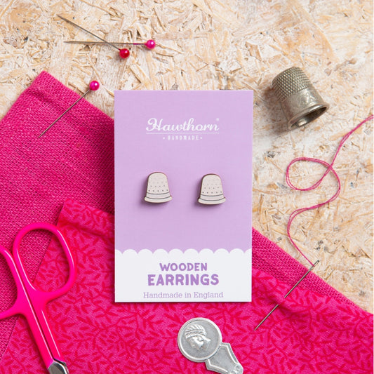 Pair of wooden earrings on a purple card with sewing tools and fabric in the background