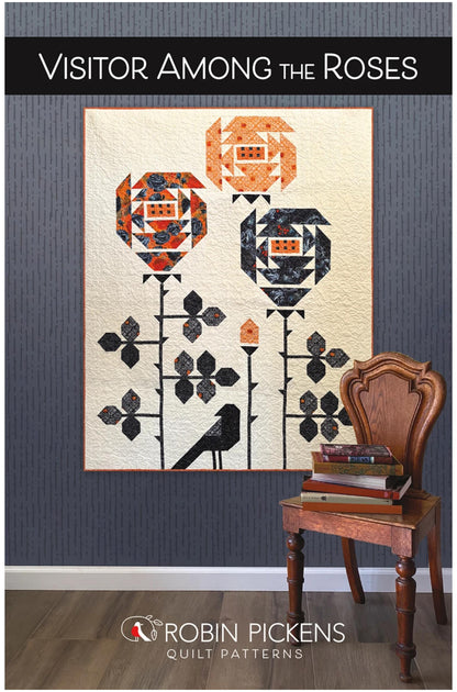 A quilt pattern cover for 'Visitor Among the Roses' by Robin Pickens Quilt Patterns, showing a floral quilt hanging on a dark gray wall next to a wooden chair with books.