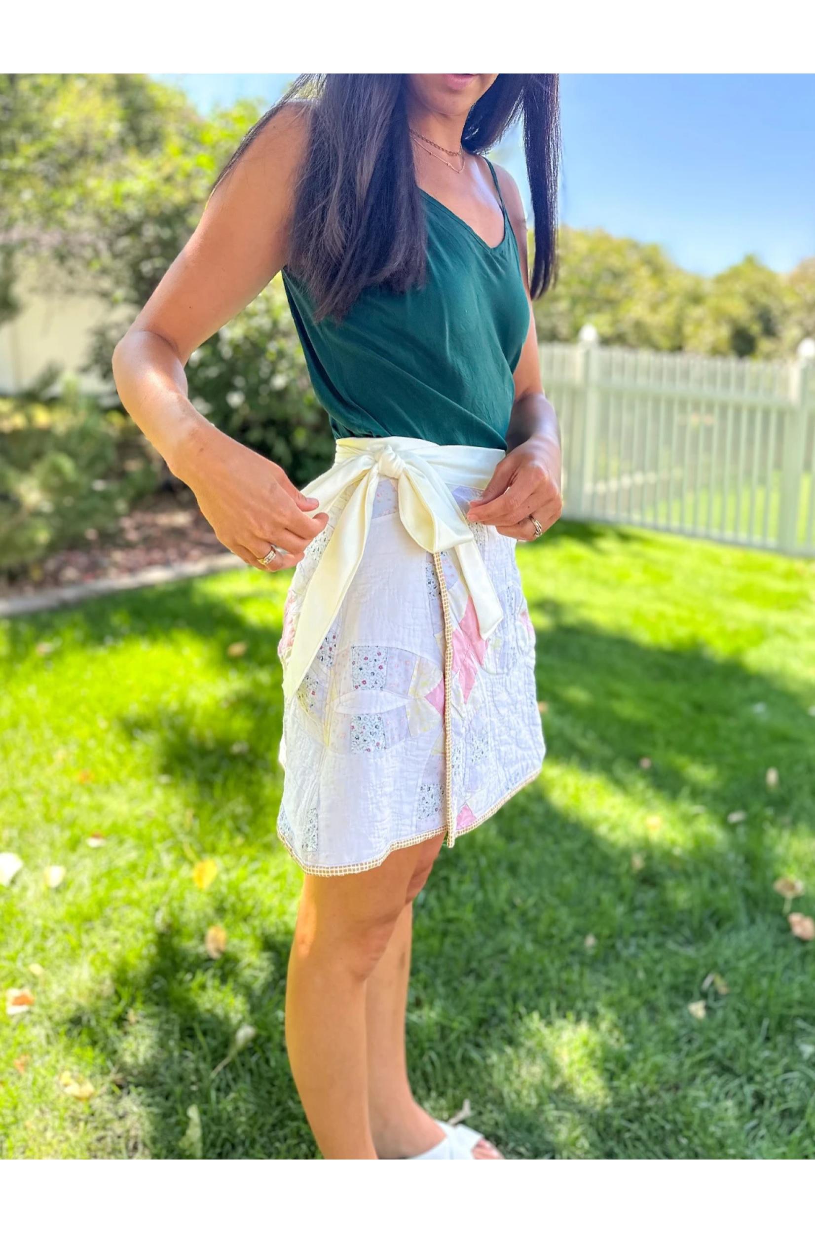 Woman wearing a green top and white lace skirt with floral patterns outdoors.