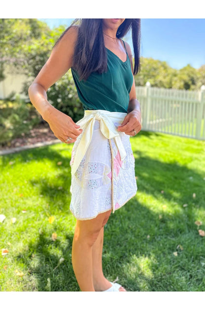 Woman wearing a green top and white lace skirt with floral patterns outdoors.
