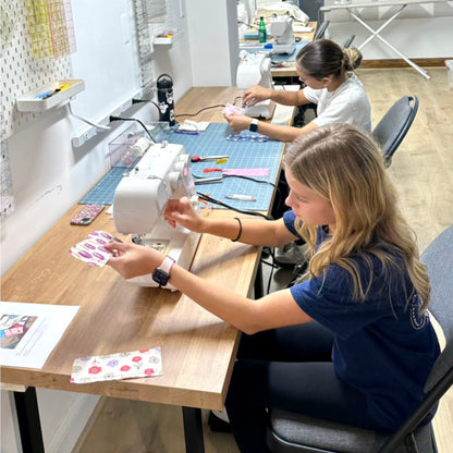 Two women working on sewing projects in a workshop setting.