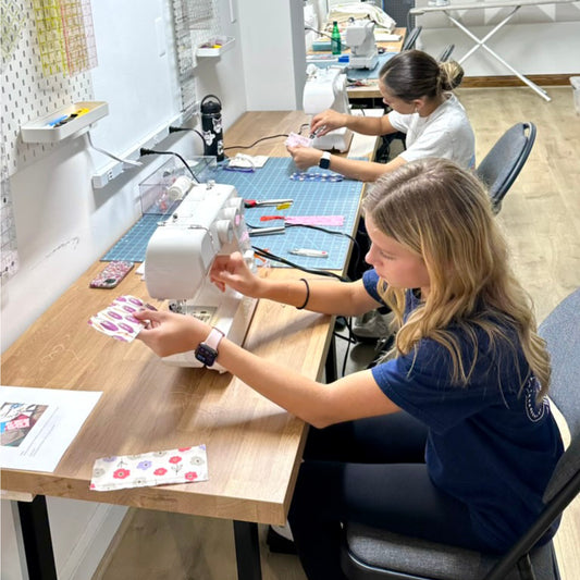 Two women working on sewing projects in a workshop setting.