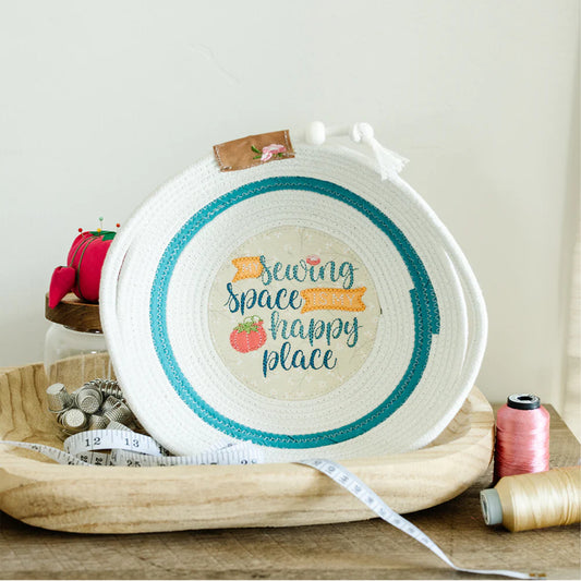 Decorative hoop with 'Sewing Space Happy Place' text on a wooden surface with sewing supplies.
