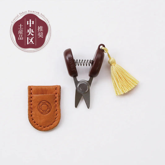 Small pair of scissors with a brown leather case and yellow tassel on a white background.