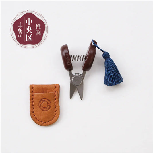 Small scissors with a leather case and tassel on a white background