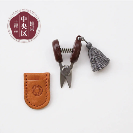 Small scissors with a leather case and tassel on a white background