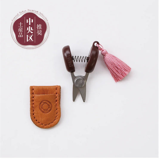 Small scissors with a brown leather case and pink tassel on a white background