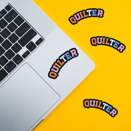 Colorful 'QUILTER' stickers on a laptop and yellow background