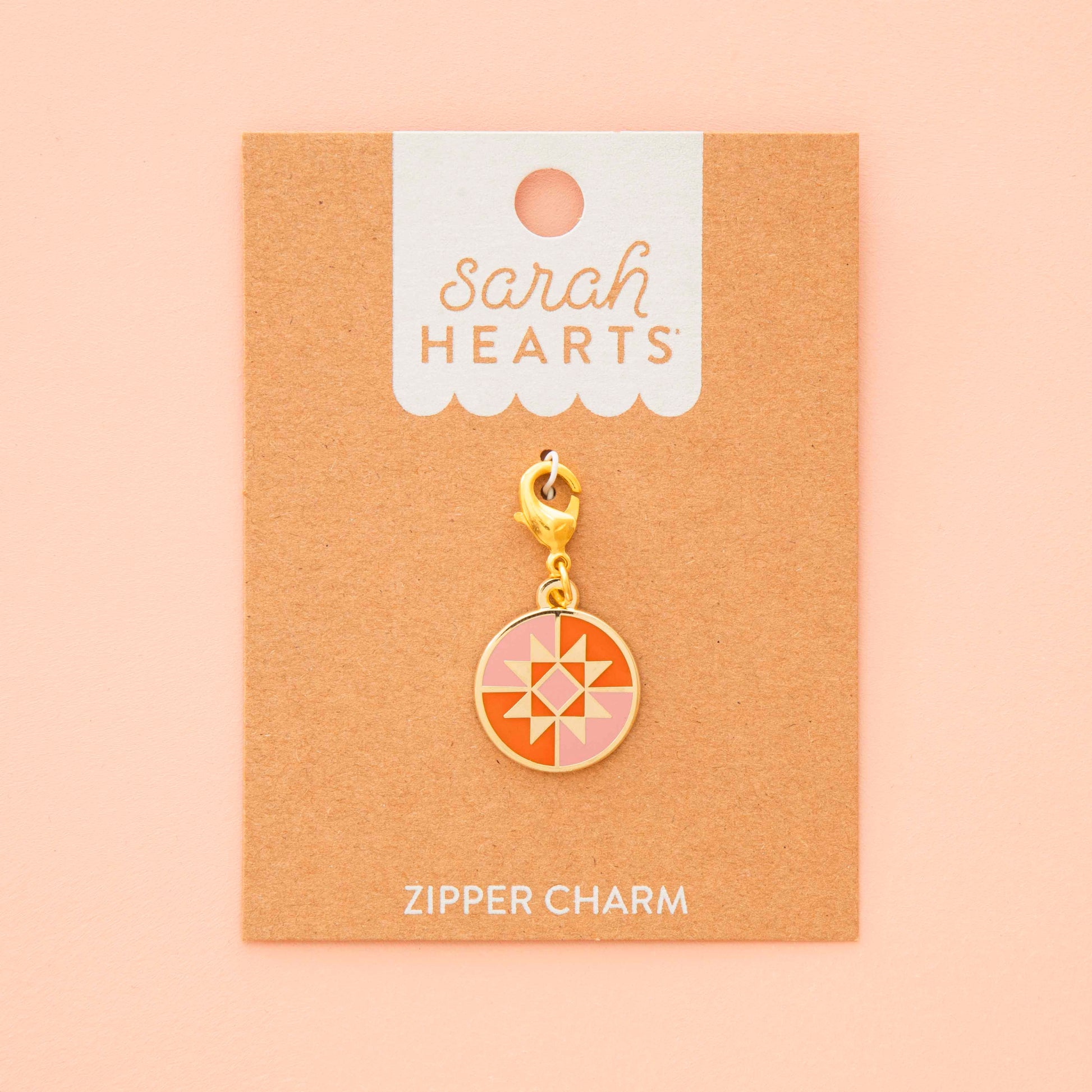 Gold zipper charm on a 'Sarah Hearts' branded card against a beige background