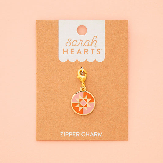 Gold zipper charm on a 'Sarah Hearts' branded card against a beige background