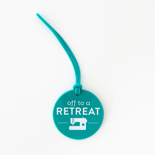 Teal luggage tag with 'off to a RETREAT' text and sewing machine icon on a white background
