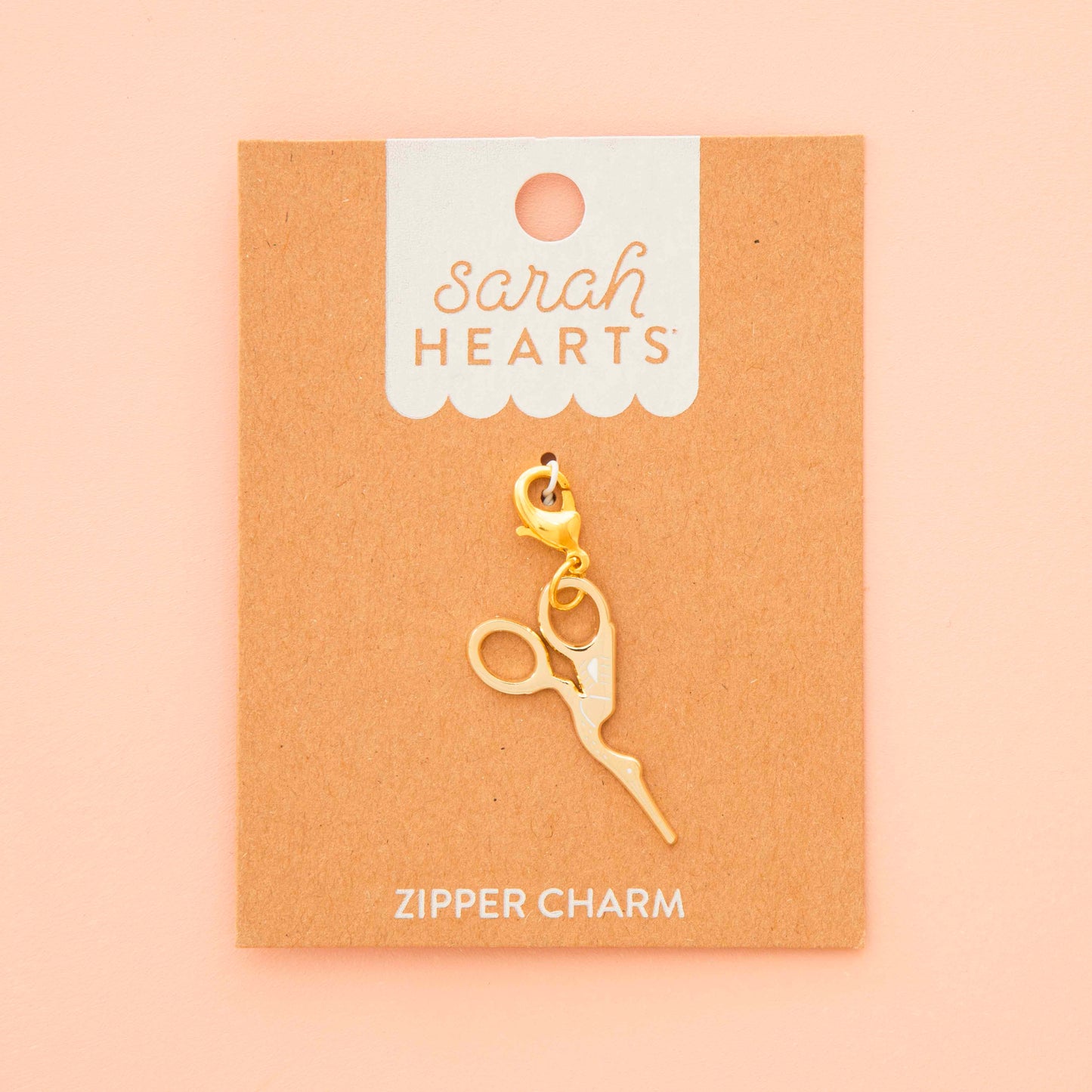 Gold zipper charm on a 'Sarah Hearts' branded card against a beige background