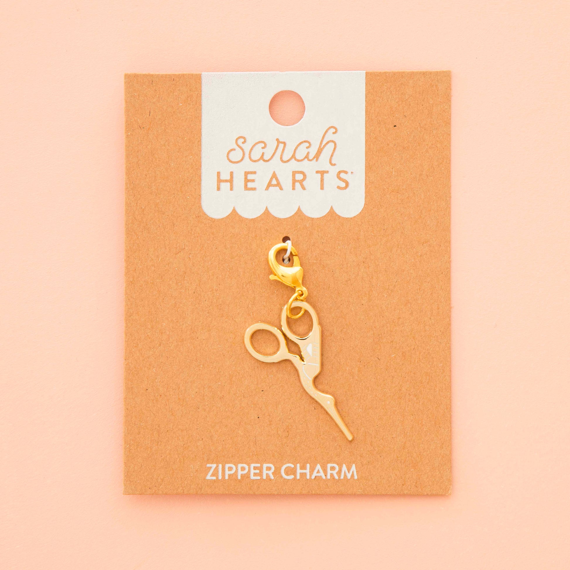 Gold zipper charm on a 'Sarah Hearts' branded card against a beige background