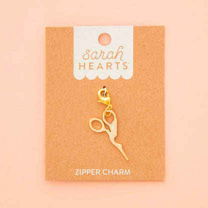 Gold zipper charm on a 'Sarah Hearts' branded card against a beige background