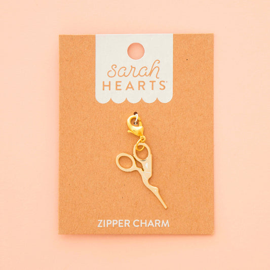 Gold zipper charm on a 'Sarah Hearts' branded card against a beige background